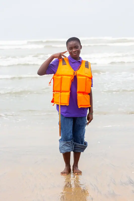 A pupil in a life jacket saluting on the beach