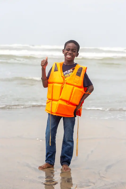 A pupil in a life jacket giving a thumbs up in the surf