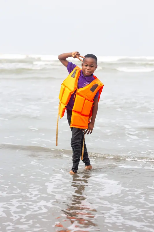 A pupil in a life jacket wading in the surf