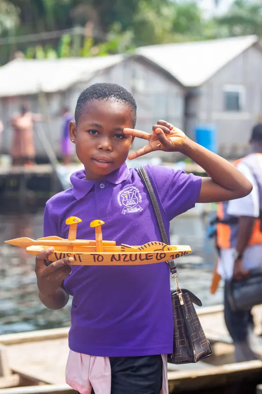 A pupil holding a carved 'Welcome to Nzulezu' model canoe