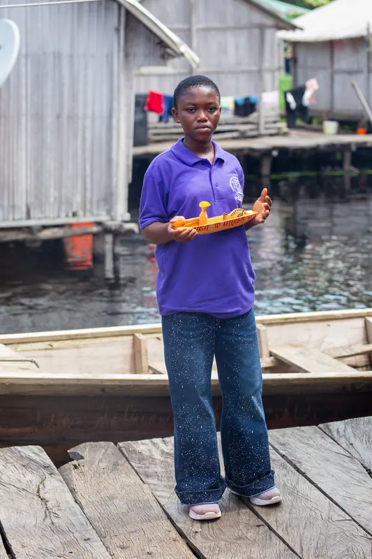 A pupil with a carved model canoe on the village walkway